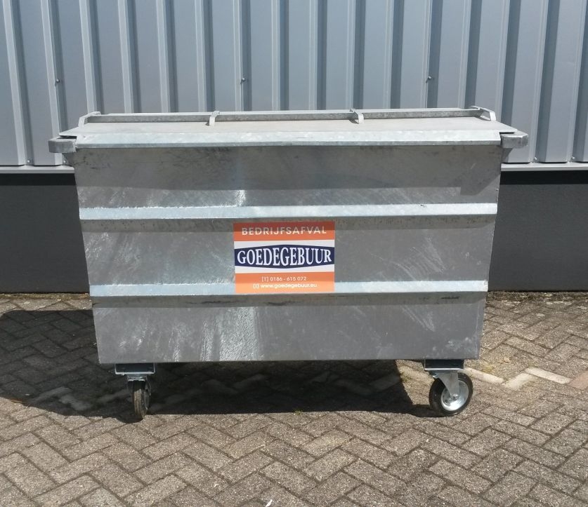 Een gegalvaniseerde afvalcontainer met deksel en zwenkwielen en de opdruk bedrijfsafval en Goedegebuur, op een verhard erf