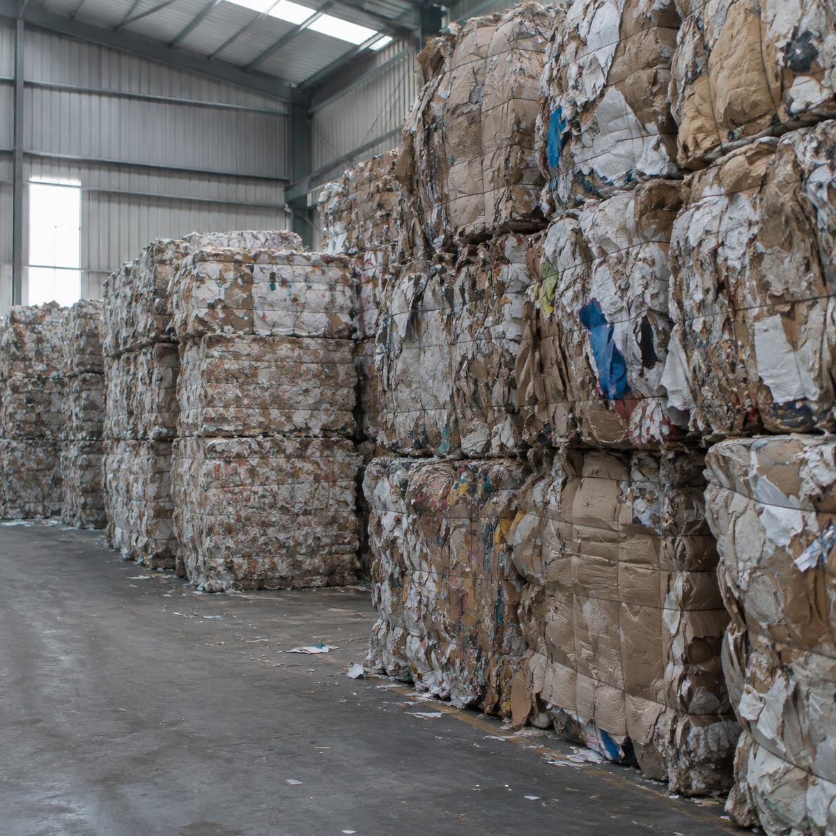 Geperste balen oud papier opgestapeld in een recyclinghal